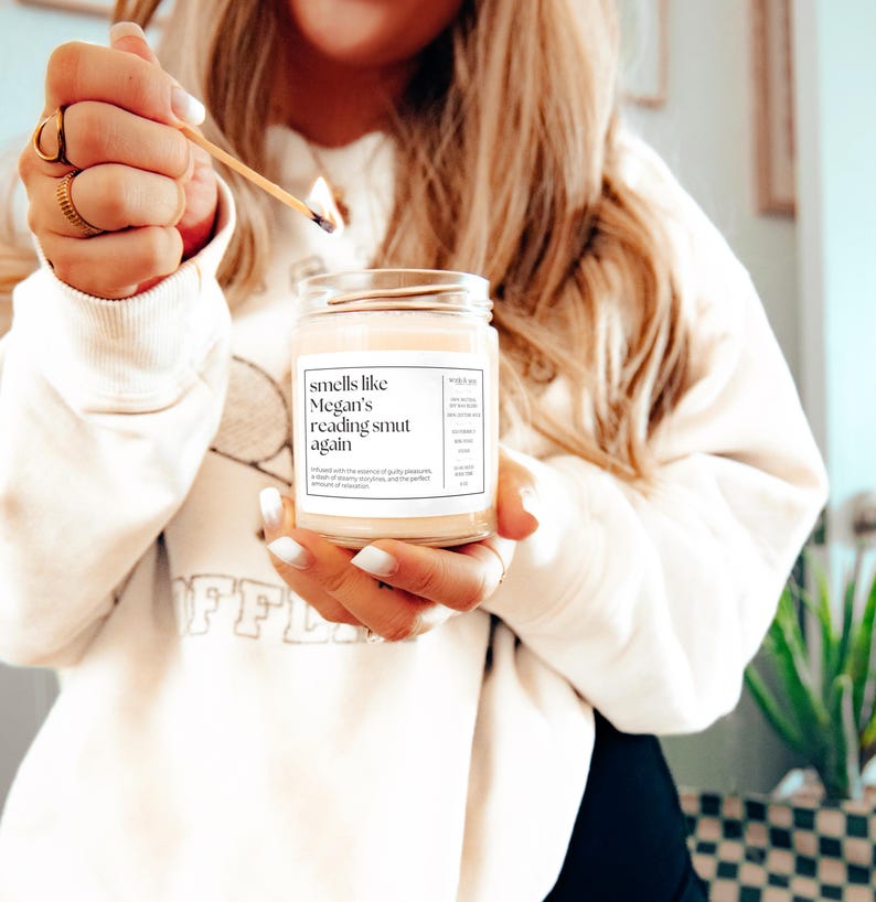 Op de afbeelding: Een witte kaars met een label waarop staat "smells like Megan's reading smut again".