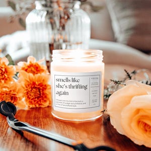 May include: A candle in a glass jar with a white label that reads "smells like she's thrifting again"  Infused with the thrill of the hunt, a sprinkle of budget-savvy brilliance, and a hint of secondhand style.