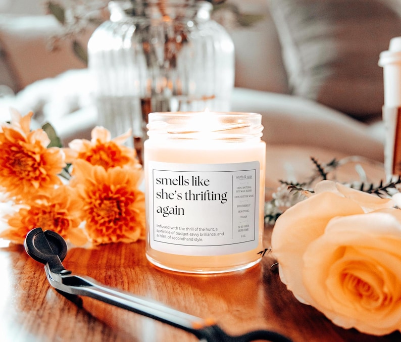 May include: A candle in a glass jar with a white label that reads "smells like she's thrifting again"  Infused with the thrill of the hunt, a sprinkle of budget-savvy brilliance, and a hint of secondhand style.