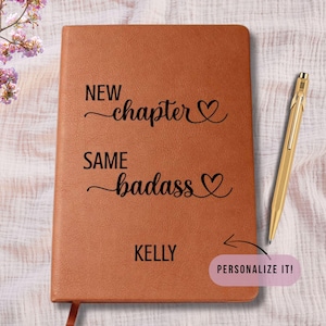 May include: A brown journal with the text "NEW chapter, SAME badass" and the name "KELLY" printed on the cover. A gold pen rests on the right side. The journal has a ribbon bookmark. A pink sticker says "PERSONALIZE IT!"