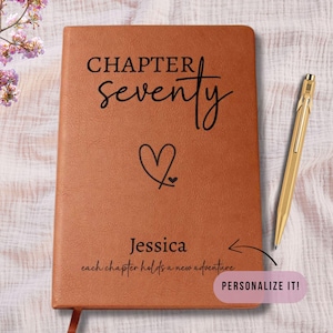 May include: A brown leather journal with the words "CHAPTER seventy" and a heart symbol. The name "Jessica" is below the heart, with the phrase "each chapter holds a new adventure." A gold pen rests beside the journal. The text "PERSONALIZE IT!" is in a pink box.