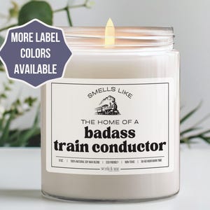 May include: A white candle with a black label that reads "Smells Like The Home of a Badass Train Conductor". The label also features a black and white illustration of a train.