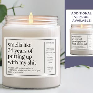 May include: A white candle with a soy wax blend and a cotton wick. The candle has a humorous message that reads "smells like 24 years of putting up with my shit." The text is infused with endless patience, unconditional love, and a touch of "you deserve an award."