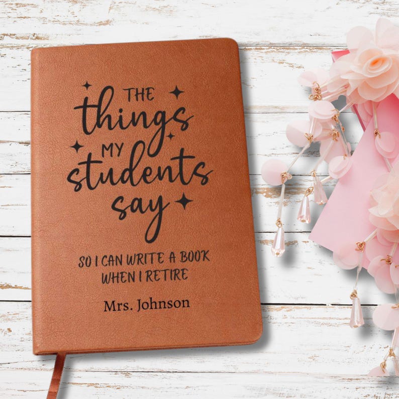 May include: A brown leather-bound notebook with the text "The things my students say" in black script. The notebook also includes the text "So I can write a book when I retire" and "Mrs. Johnson".