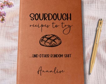 May include: A brown notebook with the text "SOURDOUGH recipes to try" and "...AND OTHER RANDOM SHIT". The notebook has a drawing of a loaf of bread and the name "Annalise" at the bottom. A gold pen rests on the right side.