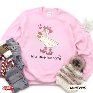 Puede incluir: Sudadera rosa con un dibujo animado de un ganso con un sombrero de vaquero y sosteniendo una taza de café. El texto "Will Mand for Coffee" está impreso debajo del ganso.