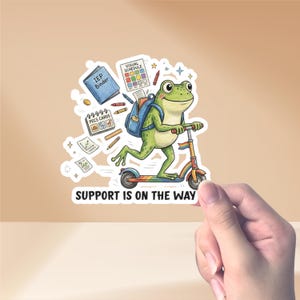 May include: A sticker depicting a green cartoon frog on a scooter with a rainbow deck. The frog has a backpack and school supplies. The text "SUPPORT IS ON THE WAY" is at the bottom of the sticker.
