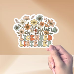 Puede incluir: Una pegatina con un diseño floral y el texto "LICENSED LISTENER". La pegatina tiene un borde blanco y una variedad de flores en tonos naranja, amarillo y azul. El texto está en una fuente retro.