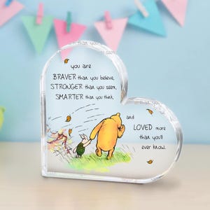 May include: A clear heart-shaped acrylic paperweight with a Winnie the Pooh and Piglet illustration. The paperweight features the quote "You are braver than you believe, stronger than you seem, smarter than you think, and loved more than you'll ever know."
