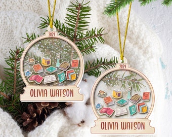 May include: Two wooden Christmas ornaments with a clear center, featuring miniature books, a coffee cup, and a vase. The ornaments have the name "OLIVIA WATSON" and the year "2024" on them. Gold string for hanging.