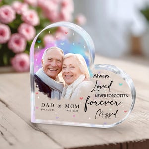 Puede incluir: Un pisapapeles de cristal en forma de corazón con una foto de una pareja mayor en su interior. El texto dice "Always Loved Never Forgotten Forever Missed" con las fechas "1933-2023" y "1942-2021" debajo de la foto.