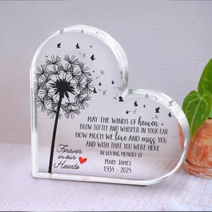 Puede incluir: Placa conmemorativa transparente en forma de corazón con un diseño de diente de león y la frase "Forever in our Hearts". La placa incluye una inscripción sobre el amor y la pérdida, con el nombre Mary James y las fechas 1934-2024.