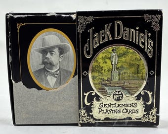 May include: Black playing card box featuring a portrait of a man in a hat and a box with the words "Jack Daniel's" and "Gentlemen's Playing Cards." The boxes have gold and white accents.