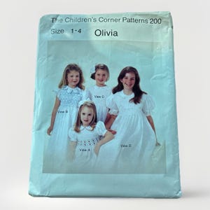 Könnte beinhalten: Ein Vintage-Schnittmuster mit dem Titel "The Children's Corner Patterns 200" mit vier Mädchen in weißen Kleidern. Das Muster ist für die Größen 1-4 und heißt "Olivia". Die Kleider haben unterschiedliche Ärmel- und Ausschnittdesigns.