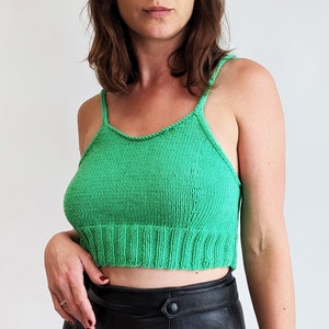 Op de afbeelding: Een vrouw draagt een felgroen gebreid crop top met dunne bandjes. Het topje heeft een geribbelde zoom en is gemaakt van een zacht, lichtgewicht garen.