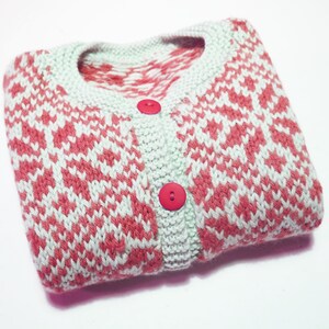 May include: A folded pink and white knitted cardigan with a geometric pattern and red buttons.