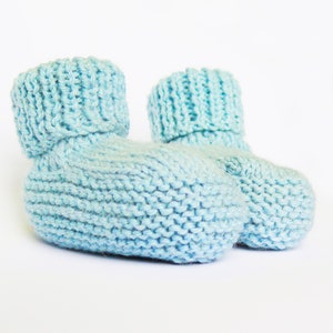 May include: A pair of light blue knitted baby booties. The booties are made of a soft, textured yarn and have a fold-over cuff.