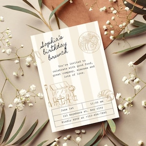 May include: A beige and brown striped invitation card with a black handwritten text that says "Sophia's birthday brunch". The card has a drawing of a cafe with a sign that says "Cafe". The card also has a drawing of a croissant and a glass of champagne. The text on the card says "You're invited to celebrate with good food, great company, mimosas and lots of love. June 1st 11:00 am 123 Anywhere st, Any city Kindly RSVP at +123-456-7890"