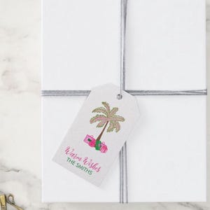 Puede incluir: Una etiqueta de regalo rosa y verde con una palmera y regalos. El texto en la etiqueta dice "Warm Wishes The Smiths".