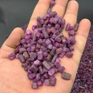 Peut inclure: Une poignée de petits cristaux de rubis violets bruts. Les cristaux sont de formes et de tailles variées, certains étant plus rectangulaires et d'autres plus arrondis.
