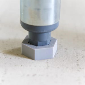 Peut inclure: Gros plan sur une base hexagonale en plastique gris pour un pied de meuble.