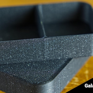 May include: Two black plastic containers with a speckled finish. The containers are stacked on top of each other. The top container has two compartments. The bottom container is a single compartment. Galaxy Black.
