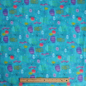 May include: Turquoise blue fabric with a repeating pattern of purple and pink jellyfish, seashells, seaweed, and stars. The fabric has the text "Swim Sweet Dreams" repeated throughout the pattern.