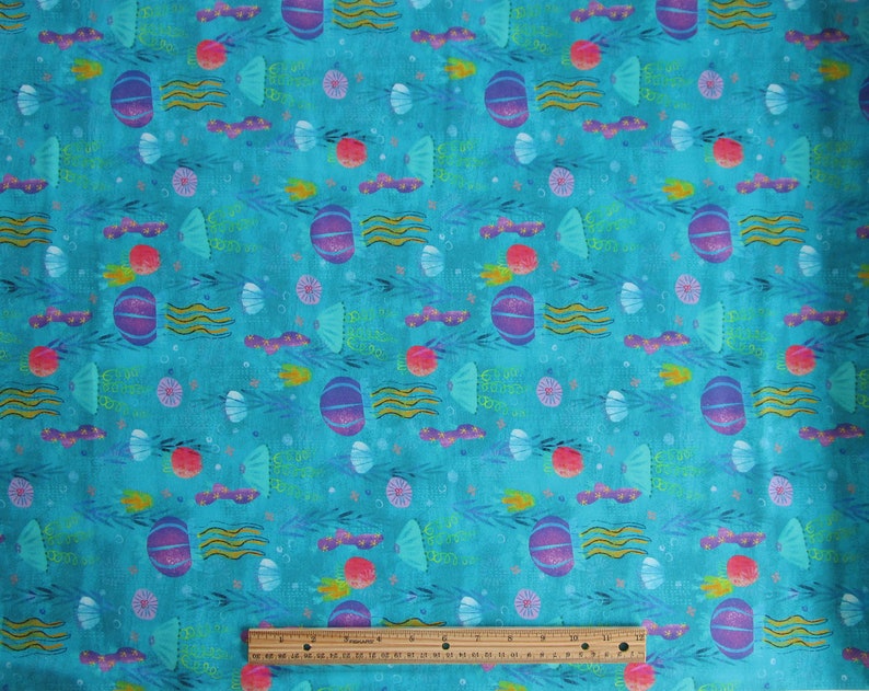 May include: Turquoise blue fabric with a repeating pattern of purple and pink jellyfish, seashells, seaweed, and stars. The fabric has the text "Swim Sweet Dreams" repeated throughout the pattern.