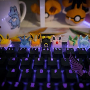 May include: A black keyboard with custom keycaps featuring various cartoon character designs. The keycaps are brightly colored and shaped like animal characters. The keyboard is lit with purple lights.