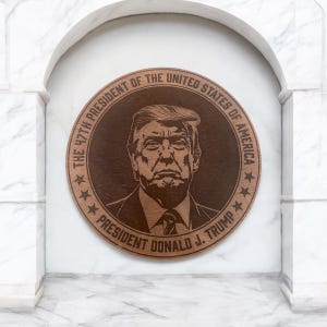 May include: A round wooden plaque with a portrait of Donald J. Trump, the 47th President of the United States of America. The plaque is brown with a dark brown border and features the text "The 47th President of the United States of America" and "President Donald J. Trump" in a white font.