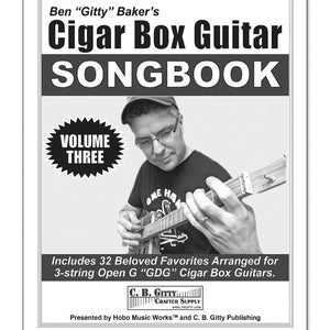 Puede incluir: Una fotografía en blanco y negro de un hombre tocando una guitarra de caja de puros. La portada de un cancionero es visible en el fondo. El cancionero se titula "Ben "Gitty" Baker's Cigar Box Guitar Songbook, Volume Three".