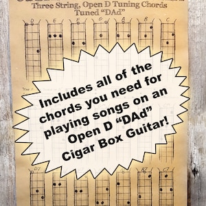 May include: A vintage-style poster with a yellow starburst graphic that says "Includes all of the chords you need for playing songs on an Open D "DAd" Cigar Box Guitar!"  The poster has a black and white diagram of a three-string cigar box guitar with the tuning "DAd" and the chords D, E, F, G, A, B, C, D7, F7, A7, B7, and C7.