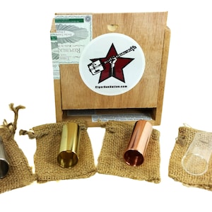 May include: Four slide guitar slides in individual burlap bags. The slides are made of stainless steel, brass, copper, and glass. The bags are arranged in a row on a white background. A wooden cigar box with a red star and the text "Cigar Box Nation.com" is in the background.