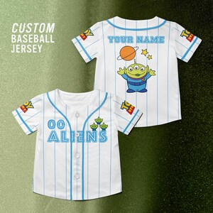Puede incluir: Dos camisetas de b&eacute;isbol blancas con finas rayas azules. Una camiseta tiene "00 ALIENS" en la parte delantera y la otra "YOUR NAME" en la parte trasera, con un dibujo de un extraterrestre y un planeta. El texto "CUSTOM BASEBALL JERSEY" est&aacute; en la esquina superior izquierda.
