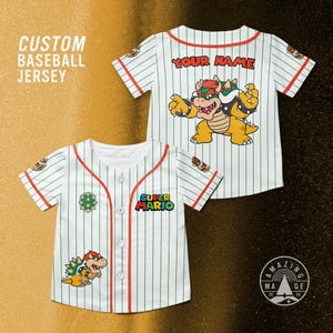 Puede incluir: Camiseta de béisbol blanca con finas rayas verdes y ribetes rojos. Presenta un gráfico de Bowser, el logotipo de Super Mario y el texto "YOUR NAME". La camiseta forma parte de una colección de camisetas de béisbol personalizadas.