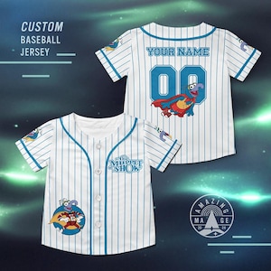 Może przedstawiać: Biała koszulka baseballowa z niebieskimi prążkami i akcentami. Koszulka zawiera napis "YOUR NAME" nad numerem "00" i postać z kreskówki. Przód koszulki ma logo "The Muppet Show" i postać z kreskówki.