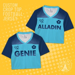 Pode incluir: Duas blusas cropped azul claro com mangas azul escuro e decote em V. Cada blusa apresenta o número "92" e um nome, "ALLADIN" e "GENIE", em azul escuro. O texto "CUSTOM CROP TOP FOOTBALL JERSEY" está no topo.