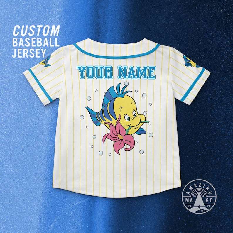 May include: White baseball jersey with yellow pinstripes, featuring a cartoon Flounder graphic and the text "YOUR NAME". The jersey has blue accents and the text "CUSTOM BASEBALL JERSEY".