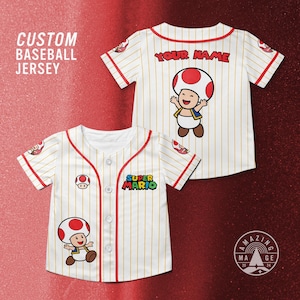 May include: White baseball jersey with red trim and pinstripes, featuring a cartoon Toad character and the text "SUPER MARIO". The jersey has the text "YOUR NAME" on the back and "CUSTOM BASEBALL JERSEY" on the side.