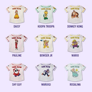 Pu&ograve; includere: Nove maglie da baseball a righe con grafiche di personaggi. Ogni maglia ha "YOUR NAME" sopra la grafica. I personaggi includono Daisy, Koopa Troopa, Donkey Kong, Pauline, Bowser Jr, Wario, Shy Guy, Waluigi e Rosalina.
