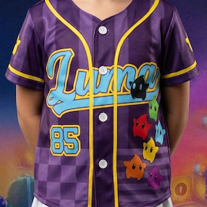 K&ouml;nnte beinhalten: Ein violettes Baseballtrikot mit Knopfleiste, das den Schriftzug "Luna" in hellblauer Schreibschrift, die Zahl "85" in Hellblau und eine vertikale Anordnung bunter sternf&ouml;rmiger Figuren in Schwarz, Gr&uuml;n, Rot, Blau, Gelb, Orange und Violett zeigt.