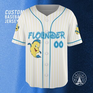 May include: White baseball jersey with yellow pinstripes and blue accents. Features the word "Flounder" in blue script, the number "00", and a cartoon image of Flounder. The text "Custom Baseball Jersey" is visible.