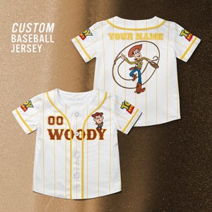 Puede incluir: Camiseta de b&eacute;isbol blanca con rayas y detalles amarillos, con el nombre "WOODY" y el n&uacute;mero "00" en la parte delantera. La parte trasera de la camiseta tiene un dibujo de vaquero de dibujos animados y el texto "YOUR NAME". La camiseta tiene el texto "CUSTOM BASEBALL JERSEY" en la parte superior izquierda.