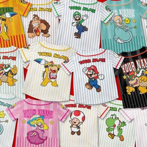 Pu&ograve; includere: Una variet&agrave; di magliette da baseball con personaggi dei cartoni animati. Ogni maglietta presenta un personaggio diverso, come Mario e Luigi, con la scritta "YOUR NAME" in alto. Le magliette hanno motivi a righe e maniche a contrasto.