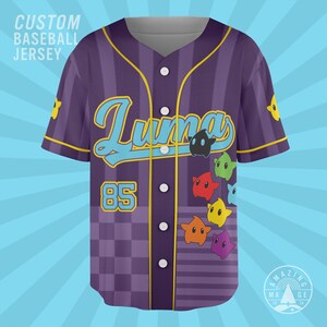May include: A purple baseball jersey featuring vertical stripes and a checkered pattern at the bottom. The front displays the text Luma in light blue, the number 85, and colorful star-shaped characters. It has a button-down front and yellow trim.