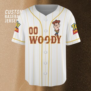 Może przedstawiać: Biała koszulka baseballowa z ż&oacute;łtymi cienkimi paskami, z postacią Woody'ego z Toy Story. Koszulka ma numer "00" i imię "WOODY" w brązowych literach. Tekst "CUSTOM BASEBALL JERSEY" jest widoczny po lewej stronie.
