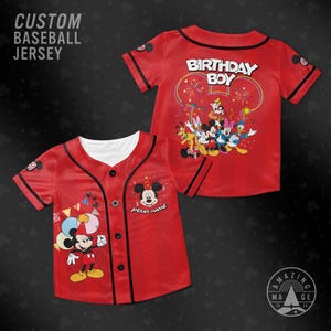 Op de afbeelding: Twee rode, op maat gemaakte honkbalshirts. Eén shirt heeft Mickey Mouse met ballonnen en de tekst "Your Name". Het andere shirt heeft "BIRTHDAY BOY" en Disney-personages. Beide hebben zwarte biezen en witte kragen.
