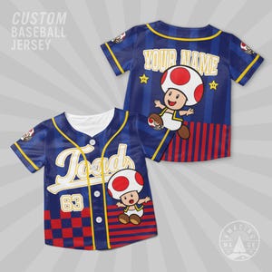 May include: Custom baseball jersey in blue with yellow trim, featuring the character Toad. The front displays "Toad" in white script and the number 63. The back has "YOUR NAME" and a Toad graphic. The jersey has a red and blue checkered pattern.