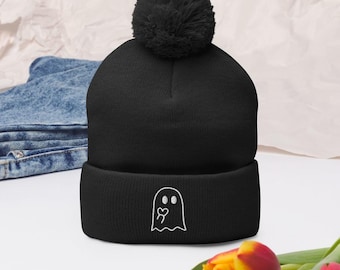 Puede incluir: Gorro negro con un fantasma bordado en blanco con un corazón. El gorro tiene un pompón negro en la parte superior.