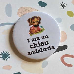 Puede incluir: Botón blanco con un perro de dibujos animados que lleva una camisa roja y blanca y una pajarita negra. El texto del botón dice "I am un chien andalusia".